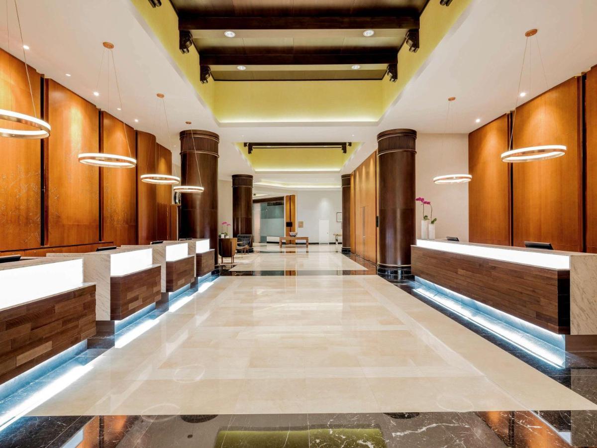 Paradox Singapore Merchant Court At Clarke Quay Экстерьер фото The photo shows a spacious and modern hotel lobby. It features several reception desks arranged along one side, each with a sleek, illuminated design. The walls are finished in warm wooden tones, and there are pendant lights hanging from the ceiling,