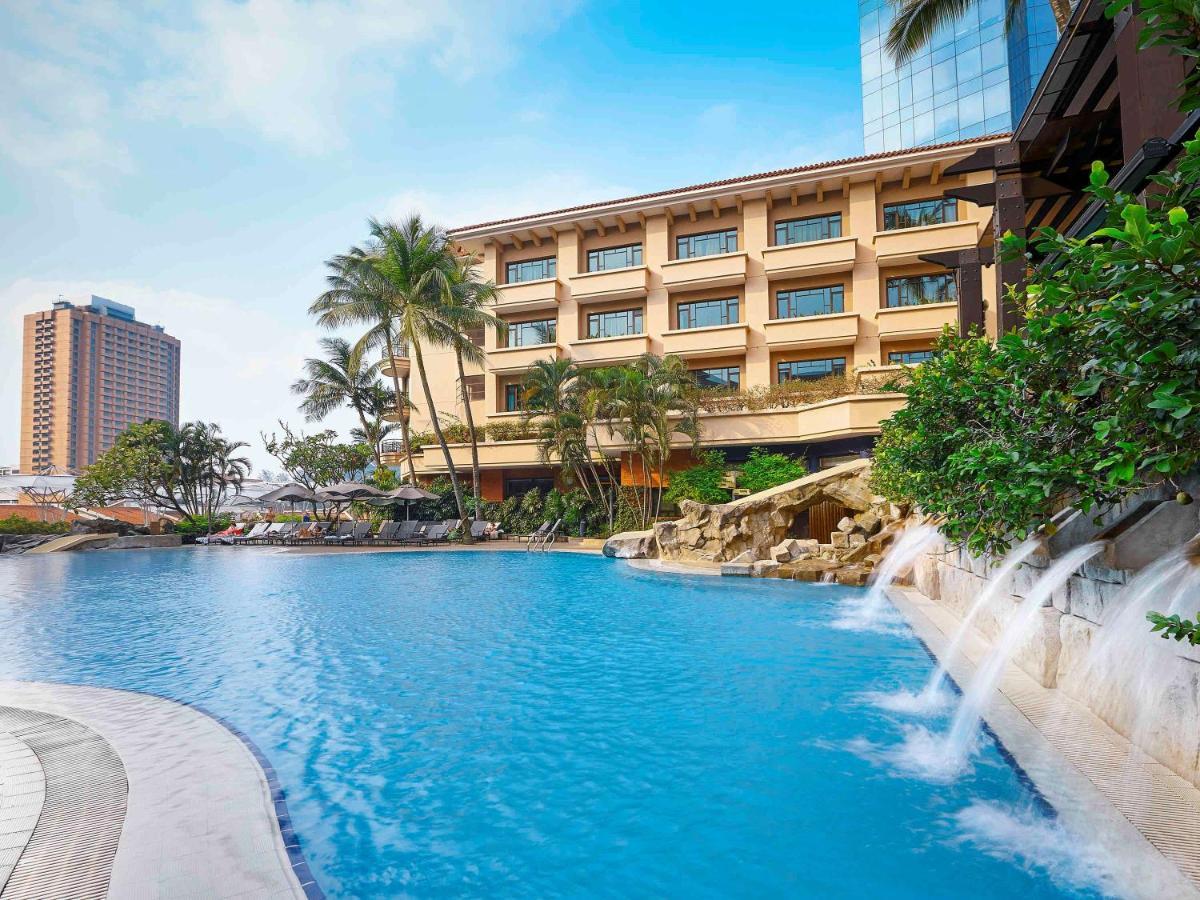 Paradox Singapore Merchant Court At Clarke Quay Экстерьер фото The photo depicts a picturesque resort featuring a large, clear blue swimming pool in the foreground. The pool is surrounded by lush greenery, including palm trees, and has waterfalls cascading into it from rocky formations. In the background, there 