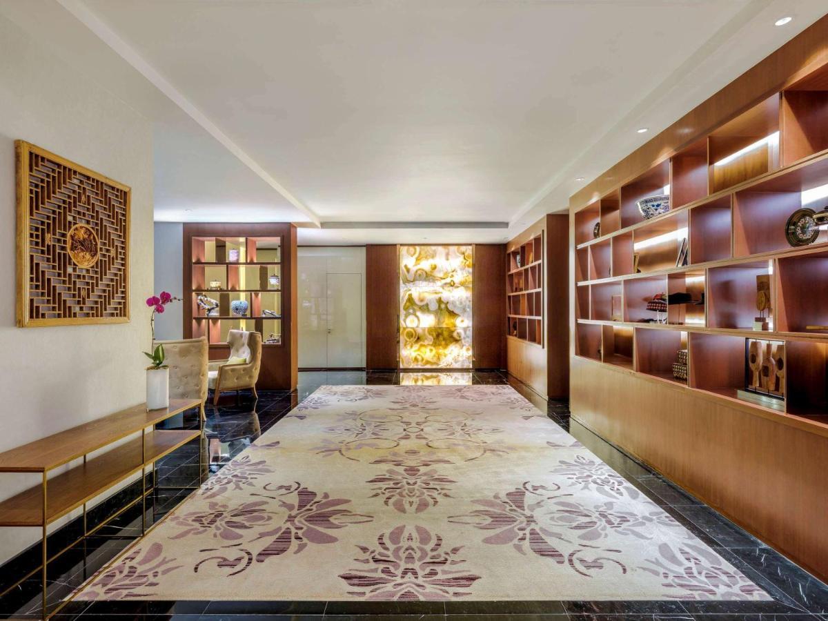 Paradox Singapore Merchant Court At Clarke Quay Экстерьер фото The photo shows a sleek and modern interior space, likely a lobby or lounge area. The floor is adorned with a large, elegant rug featuring floral patterns in soft colors. On one side, there is a wooden shelf filled with decorative items and books, al