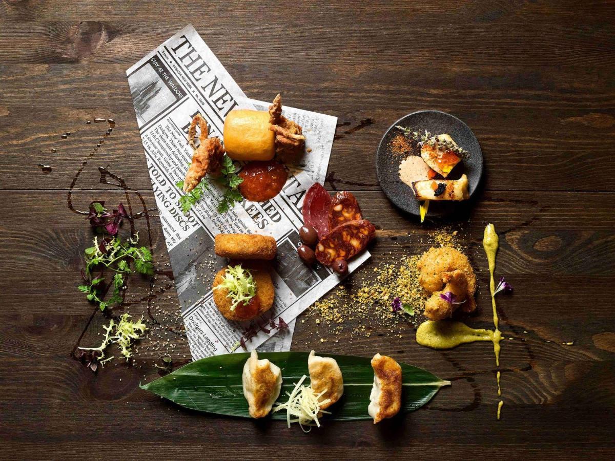 Paradox Singapore Merchant Court At Clarke Quay Экстерьер фото The photo displays an artistic arrangement of various food items on a dark wooden table. The food is positioned atop a crumpled newspaper, creating a casual yet sophisticated dining presentation. 

There are several pieces of fried food, including wh