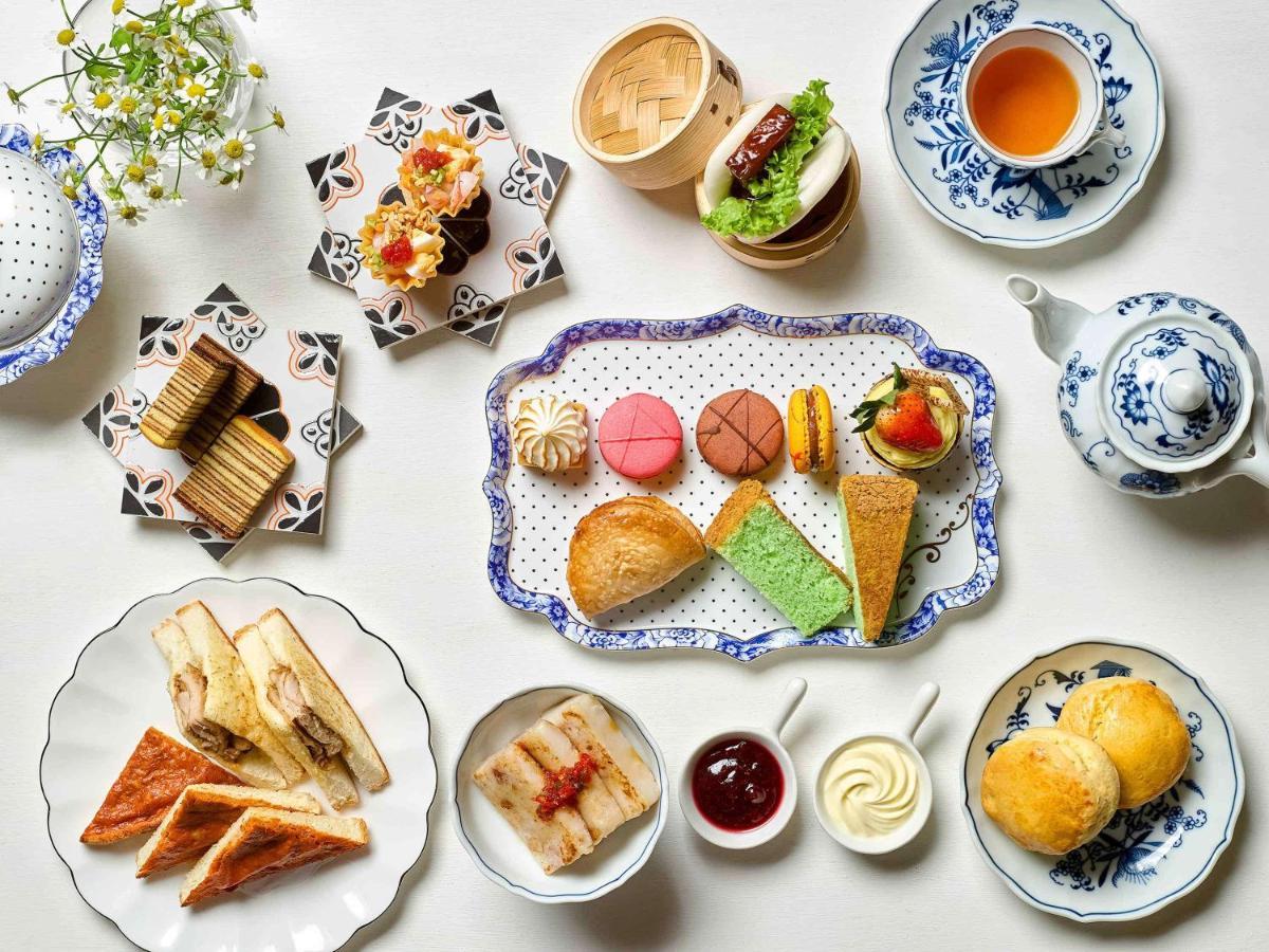 Paradox Singapore Merchant Court At Clarke Quay Экстерьер фото The photo displays a beautifully arranged assortment of food items, likely presented for an afternoon tea or dessert setting. 

- In the center, there is a decorative platter featuring a variety of pastries, including colorful macarons, small cakes, 