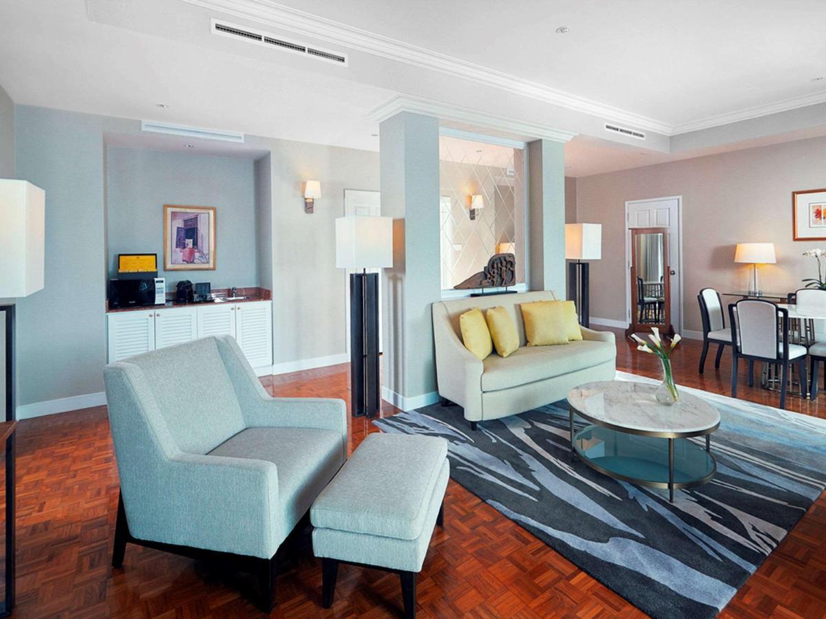 Paradox Singapore Merchant Court At Clarke Quay Экстерьер фото The photo shows a modern living space, which includes a seating area with a light-colored sofa that has yellow cushions, and an armchair with an ottoman. A round glass coffee table sits in the center on a patterned rug. In the background, there is a 