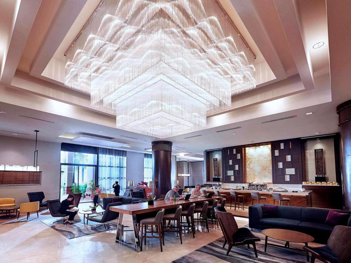 Paradox Singapore Merchant Court At Clarke Quay Экстерьер фото The photo depicts a modern, stylish lobby area. It features a striking chandelier that hangs from a high ceiling, creating a focal point above the seating areas. The furnishings include a mix of chairs and tables, with a cozy ambiance provided by var