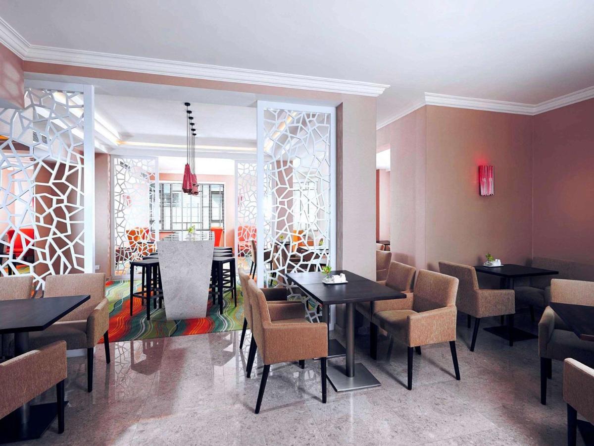 Paradox Singapore Merchant Court At Clarke Quay Экстерьер фото The photo shows a modern restaurant interior. There are several tables arranged with dark surfaces and comfortable beige chairs. The walls are painted in neutral tones, and there are decorative partition screens with an abstract pattern that adds a c