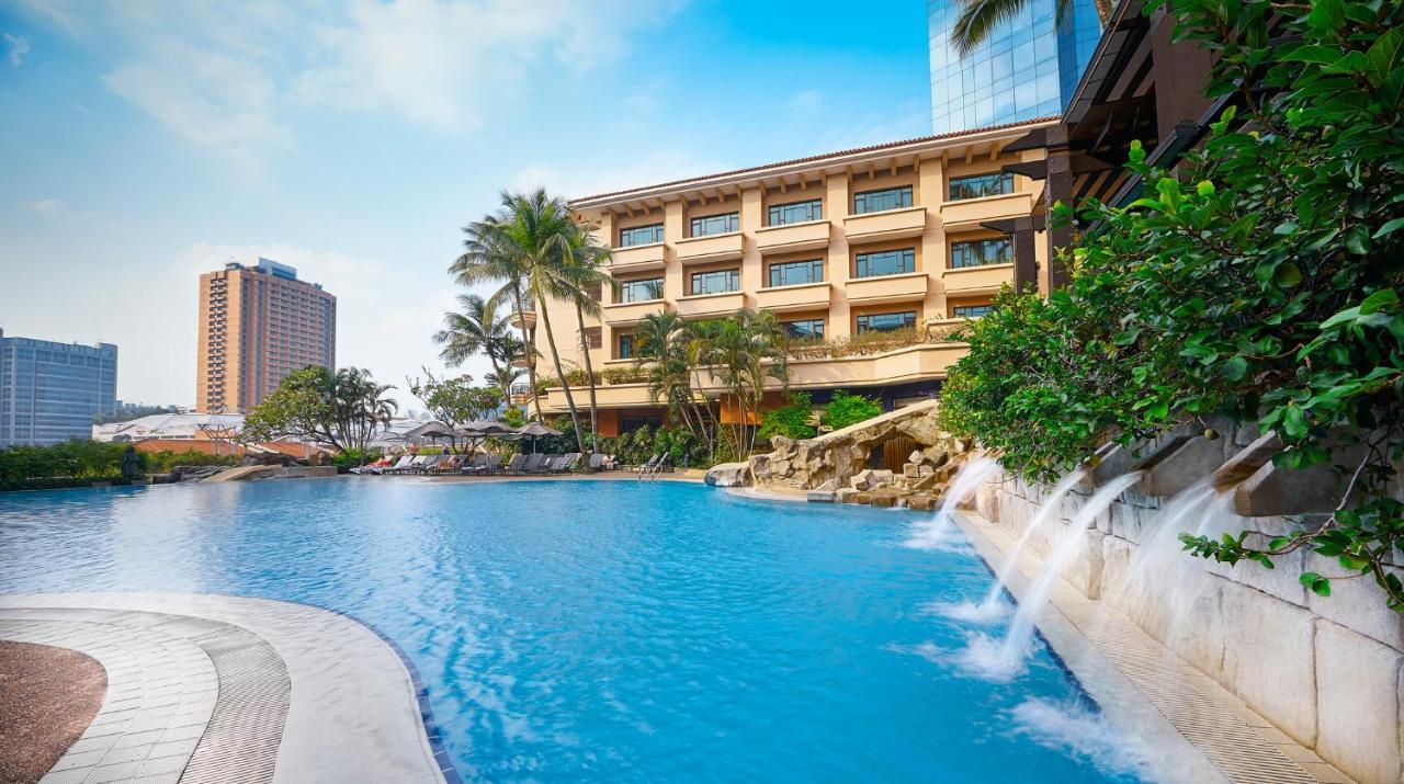 Paradox Singapore Merchant Court At Clarke Quay Экстерьер фото The photo showcases a scenic hotel resort with a large blue swimming pool in the foreground. The pool features artificial rock formations and small waterfalls cascading gently into the water. Surrounding the pool are lush tropical plants and palm tre