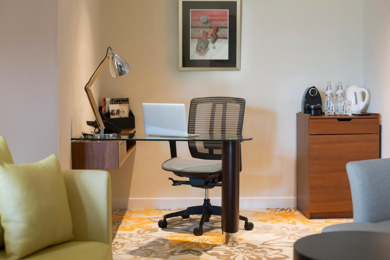 Paradox Singapore Merchant Court At Clarke Quay Экстерьер фото The photo shows a workspace setup in a well-lit room. It features a modern desk with a glass top and a comfortable office chair. On the desk, there is a laptop and a desk lamp for illumination. To the side, there are some accessories and a coffee mac