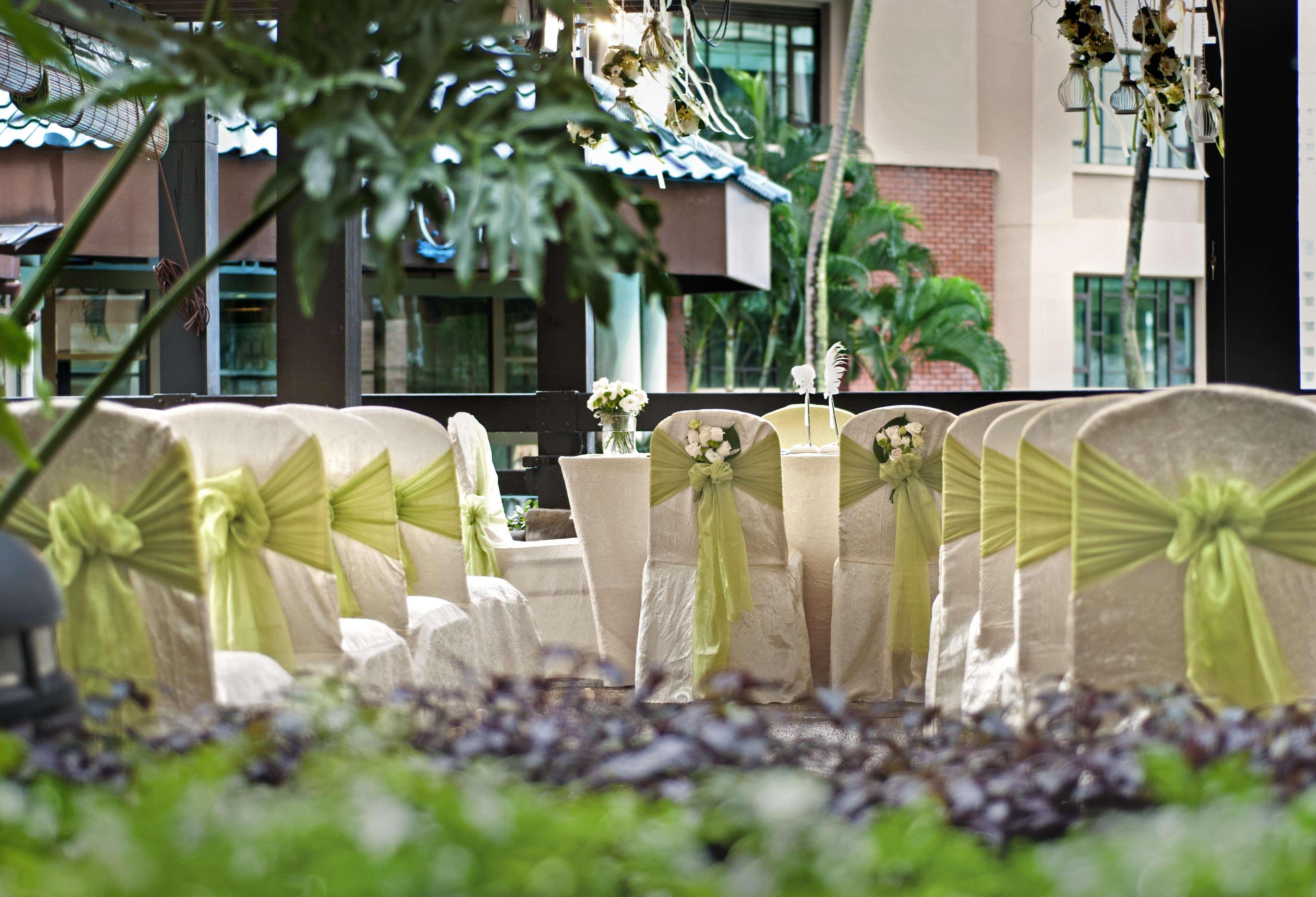 Paradox Singapore Merchant Court At Clarke Quay Экстерьер фото The photo shows a decorated setting for an event, likely a wedding or a formal gathering. There are several chairs covered in light fabric with green sashes tied around them, creating an elegant look. In the foreground, there are potted plants and gr