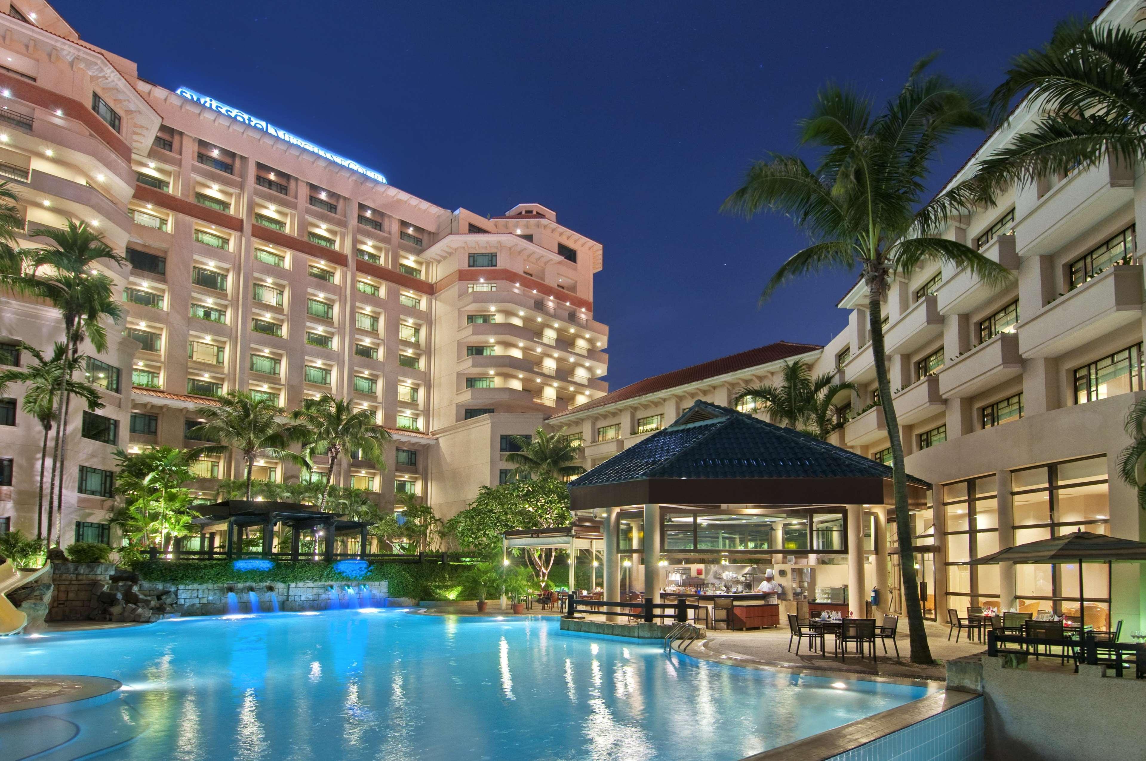 Paradox Singapore Merchant Court At Clarke Quay Удобства фото The photo depicts a modern hotel complex at night. The hotel buildings are illuminated, showcasing their architectural features. In the foreground, there is a large swimming pool, which reflects the lights from the surrounding area, creating a tranqu