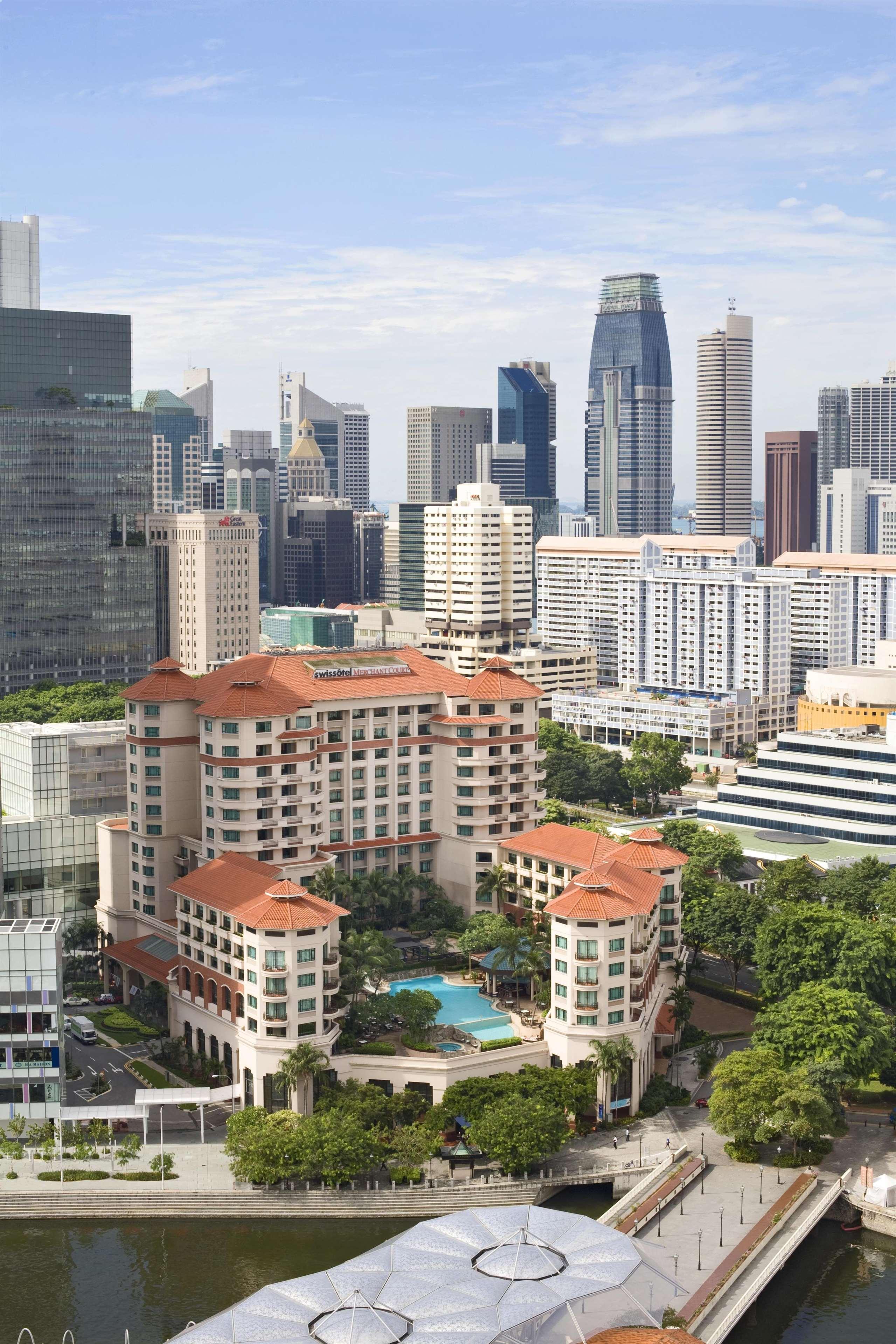 Paradox Singapore Merchant Court At Clarke Quay Экстерьер фото The photo shows a cityscape featuring a mix of modern skyscrapers and buildings. In the foreground, there is a large hotel with a distinctive architectural style, characterized by its multi-level structure and a tiled roof. Surrounding the hotel, the