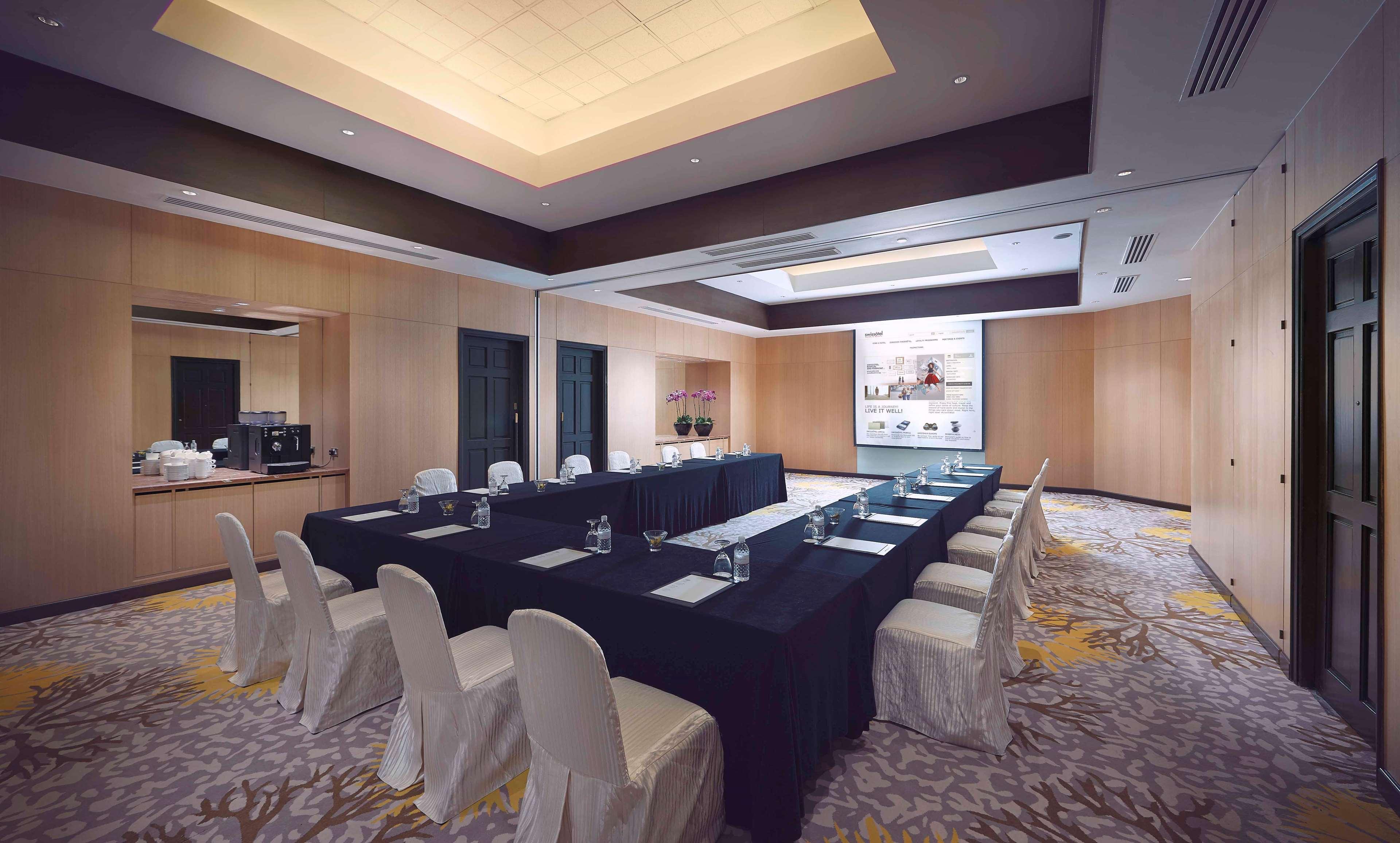 Paradox Singapore Merchant Court At Clarke Quay Экстерьер фото The photo shows a conference room designed for meetings or presentations. It features a long rectangular table covered with a black tablecloth, surrounded by white chairs. There are glass water pitchers and glasses on the table. The room has wooden p