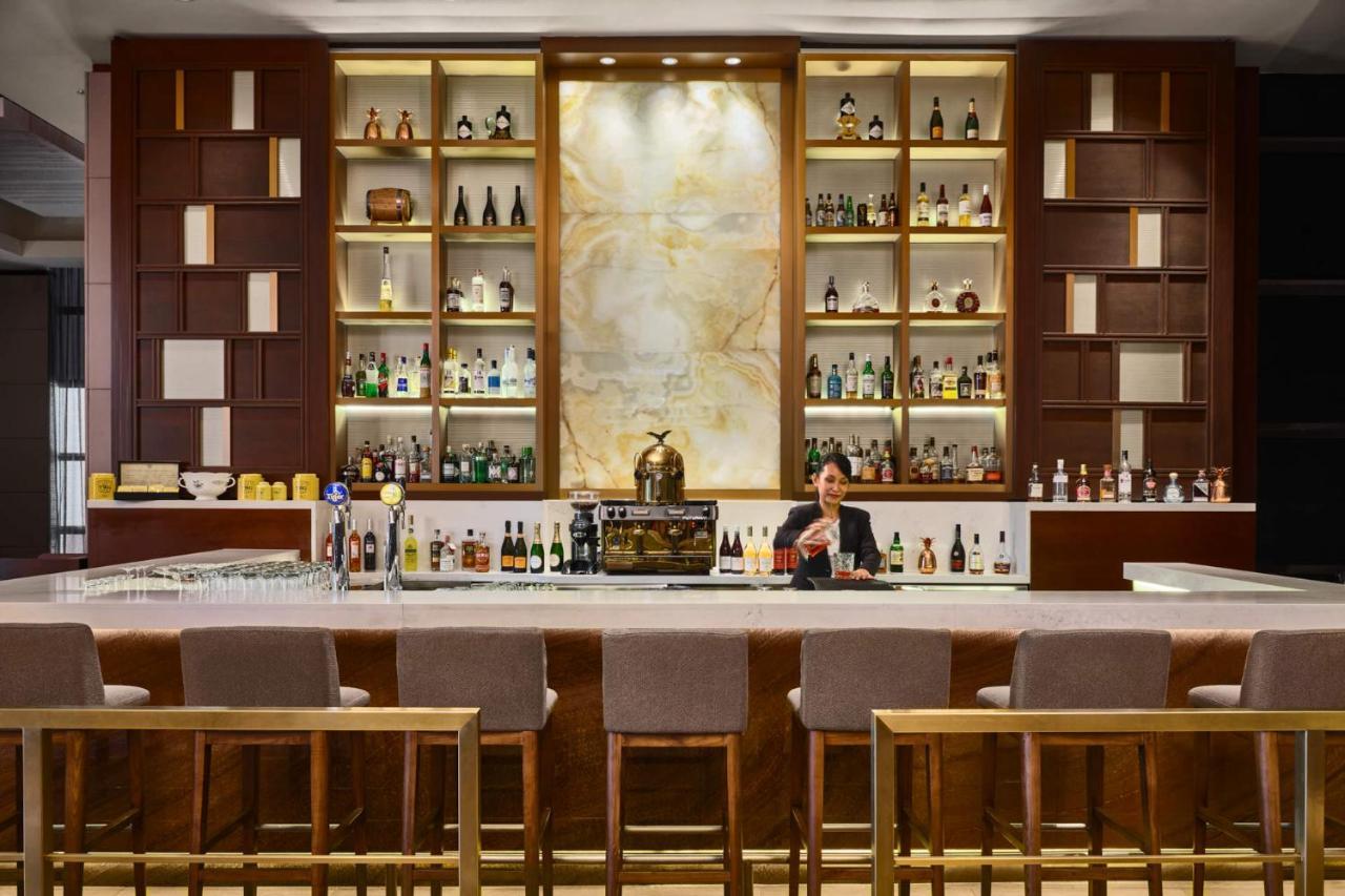Paradox Singapore Merchant Court At Clarke Quay Экстерьер фото The photo shows a well-designed bar area. The bar has a long counter with high stools arranged in front. Behind the bar, there is an elegant display of various bottles of spirits, arranged on shelves with a stylish backdrop. The shelves feature a com