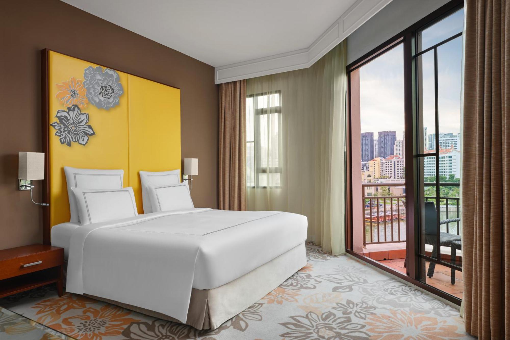 Paradox Singapore Merchant Court At Clarke Quay Экстерьер фото The photo shows a modern hotel room featuring two beds with white linens placed against a yellow accent wall adorned with decorative elements. The room has large windows with sheer curtains, allowing natural light to enter and offering a view of the 